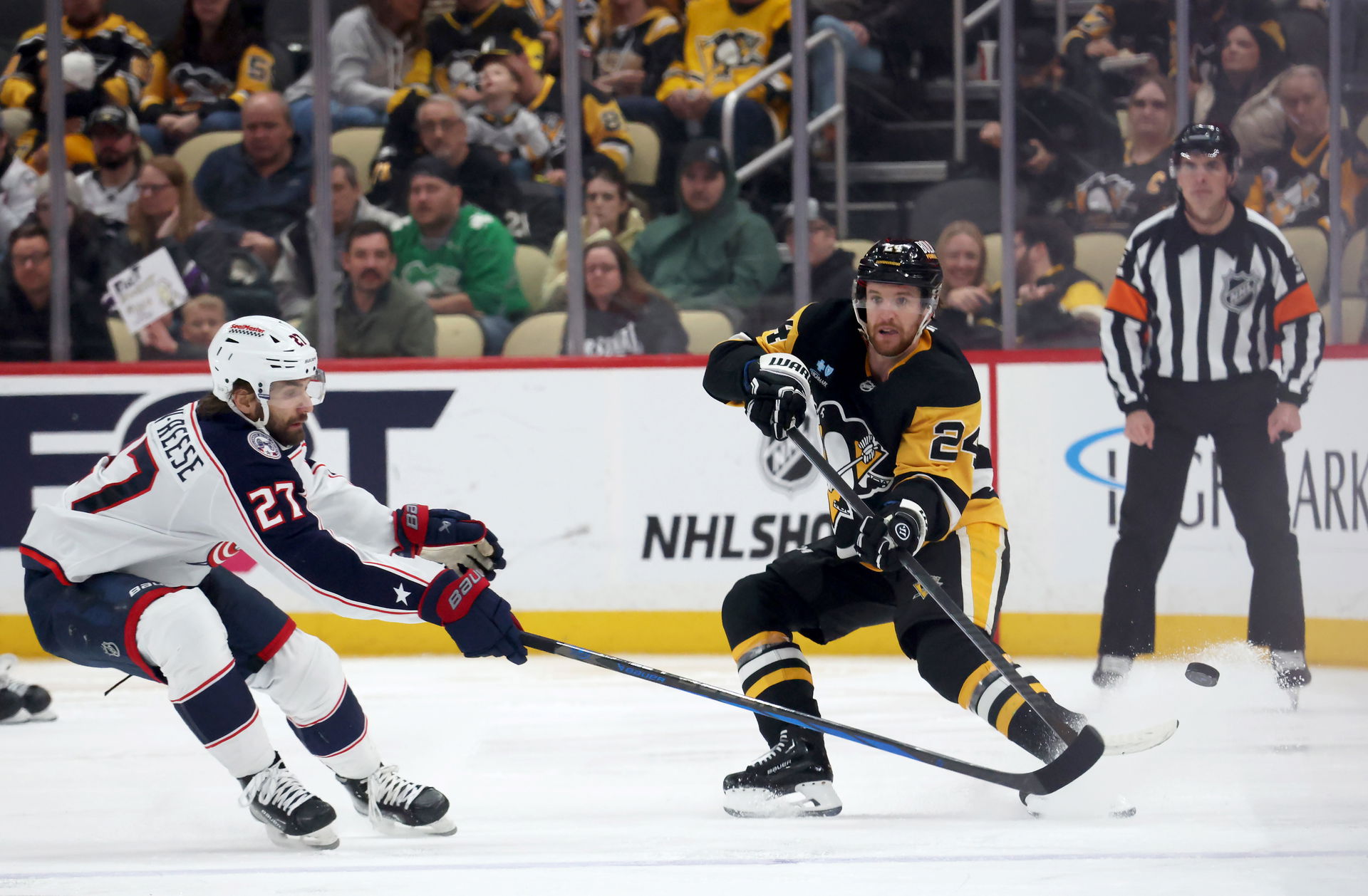 Mar 21, 2025; Pittsburgh, Pennsylvania, USA; Pittsburgh Penguins defenseman Matt Grzelcyk (24) dumps the puck up ice past Columbus Blue Jackets center Zachary Aston-Reese (27) during the third period at PPG Paints Arena. (Charles LeClaire-Imagn Images)