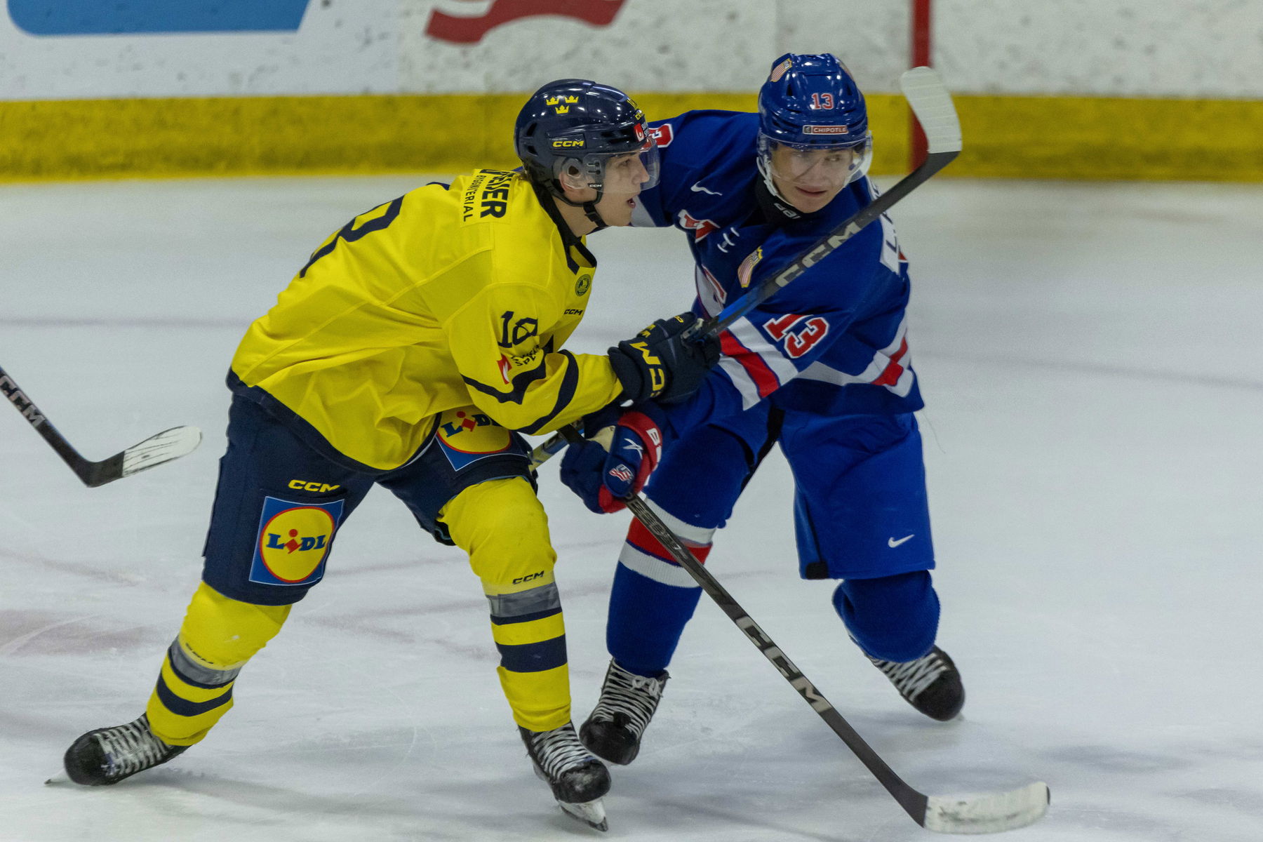 Aug 2, 2024; Plymouth, MI, USA; USA’s defenceman Lukas Fischer (13) battles for position with Sweden's forward Victor Eklund (18) during the first period of the 2024 World Junior Summer Showcase at USA Hockey Arena. Mandatory Credit: David Reginek-Imagn Images