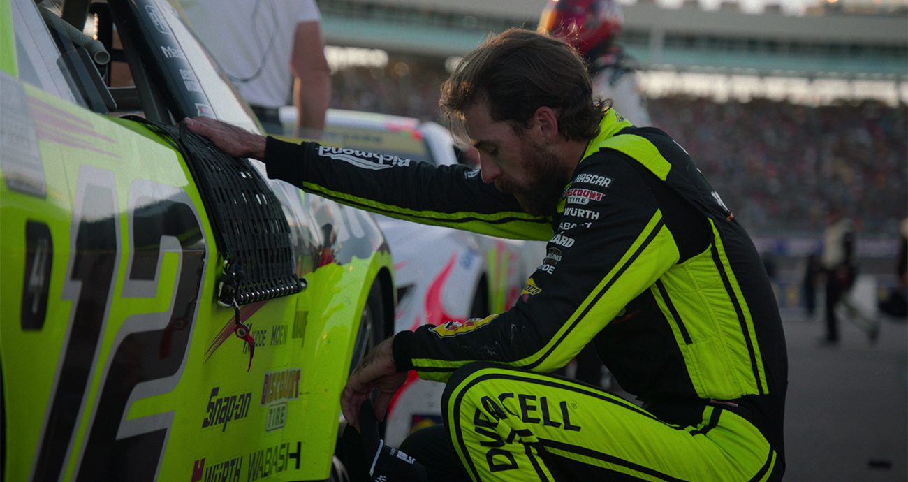 Ryan Blaney kneels next to car