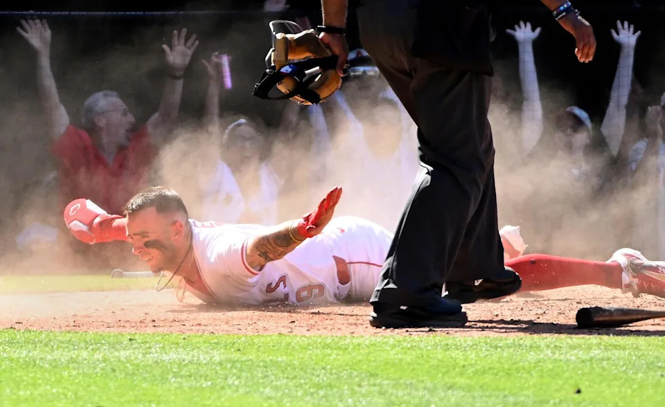 Angels shortstop Zach Neto gives the safe sign as he slides on his belly across home plate ahead of the tag.