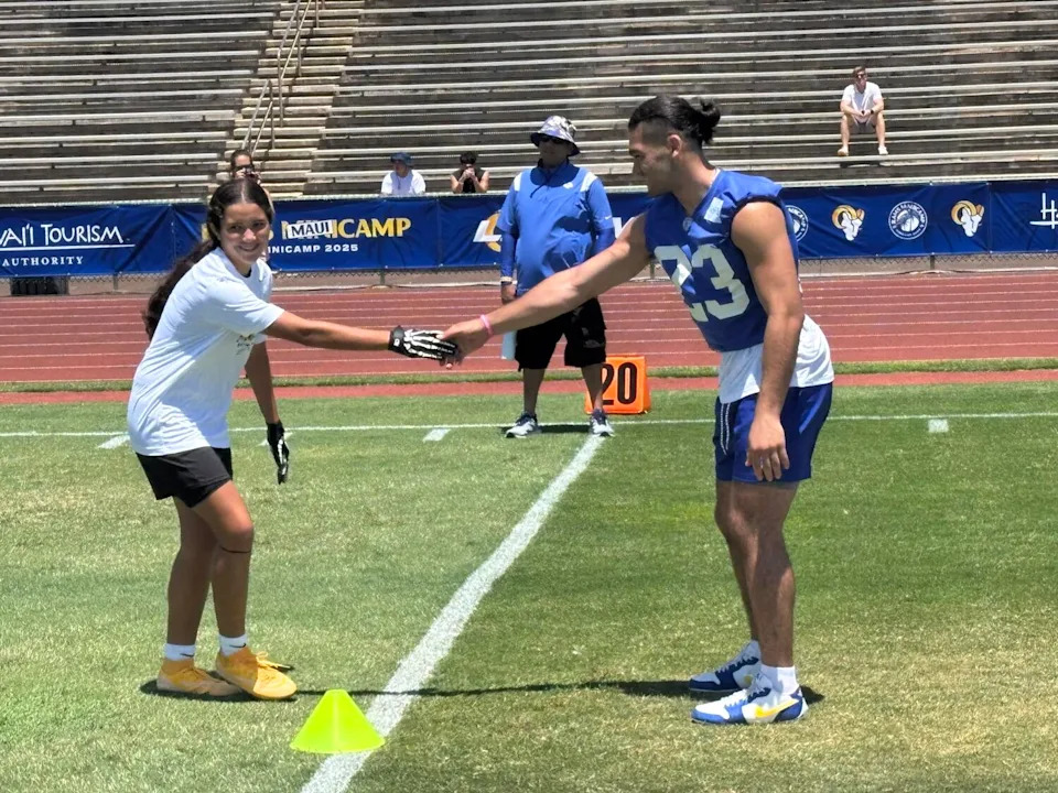 Rams wide receiver Puka Nacua shakes hands with a youth flag football player during a clinic drill.