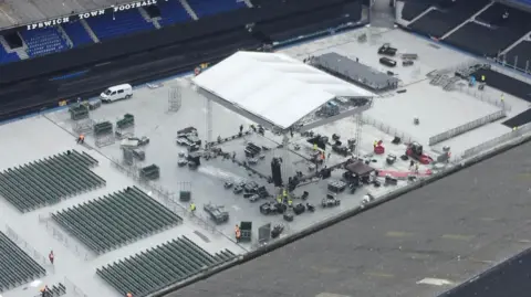 Jamie Niblock/BBC A drone shot shows a cover for a boxing ring being erected in the middle of the Portman Road stadium. A sheet has been placed over the pitch and rows of chairs placed on each side of the ring