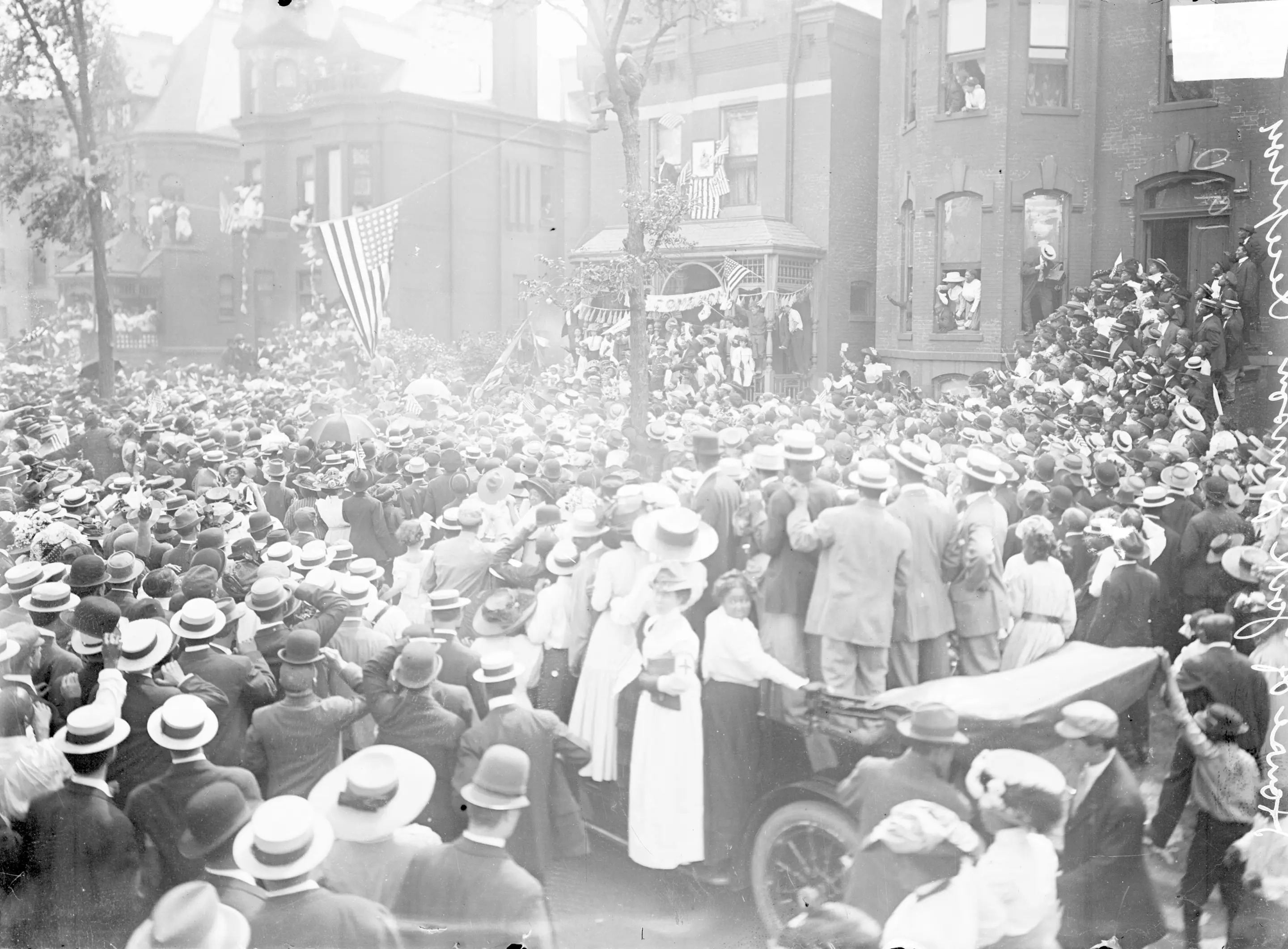 Portrait of a large crowd of people gathering on the street in front of a house where Jack Johnson's reception was taking place in Chicago, IL, 1910. Johnson was the first African American boxer to hold the title of heavyweight champion. American flags are hanging on the front of the house and strung on a line between two trees in front of the house. The crowd appears to be largely African Americans. A group of spectators are standing inside and on the running board of an automobile stopped in the street. (Photo by Chicago Sun-Times/Chicago Daily News collection/Chicago History Museum/Getty Images)