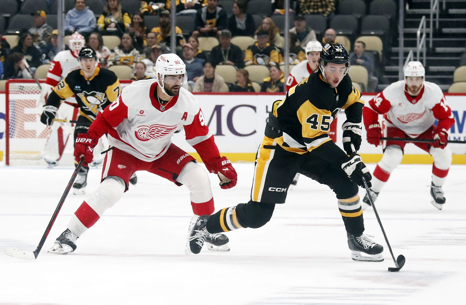 Oct 1, 2024; Pittsburgh, Pennsylvania, USA; Pittsburgh Penguins defenseman Harrison Brunicke (45) handles the puck ahead of Detroit Red Wings center Joe Veleno (90) during the second period at PPG Paints Arena. Mandatory Credit: Charles LeClaire-Imagn Images