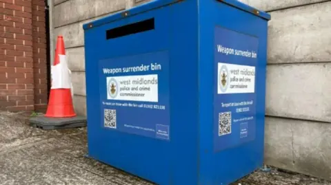 David Lumb/BBC A large blue bin with the words "weapon surrender bin" in white and bar code. A traffic cone is placed next to it and it is located outside in a car park. 