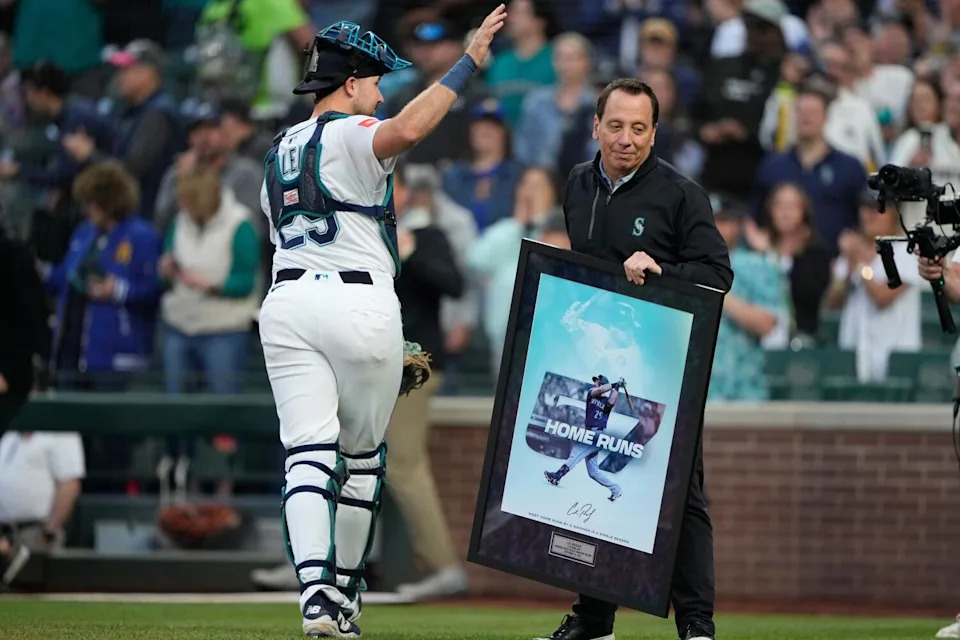 Cal Raleigh waves to the crowd as executive Kevin Martinez holds a framed poster acknowledging Raleigh's 57 home runs.