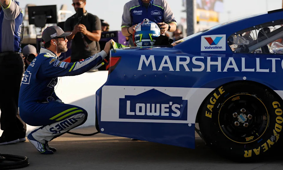 Jimmie Johnson squats behind his car as he waits to qualify for a NASCAR Cup Series auto race at Kansas Speedway in Kansas City, Kan., Friday, Oct. 20, 2017. (AP Photo/Colin E. Braley)