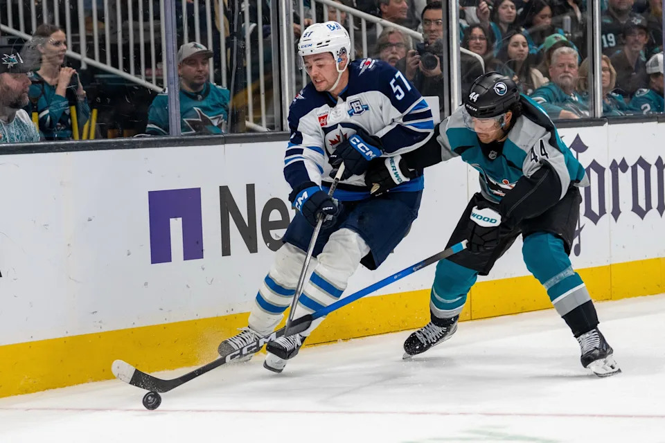San Jose Sharks left wing Kiefer Sherwood (44) and Winnipeg Jets defenseman Elias Salomonsson (57) battle for the puck against the boards.