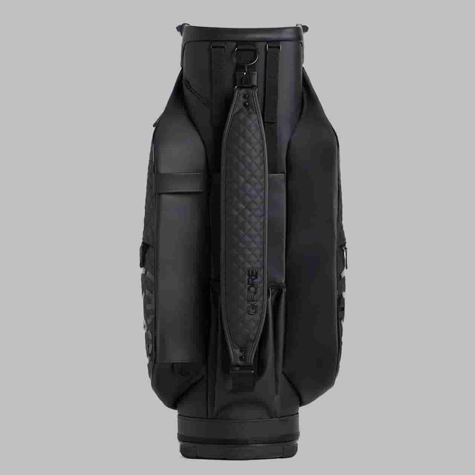 A black golf bag with a textured, padded shoulder strap stands upright against a plain gray background. With multiple compartments and a sleek, modern design, it’s set to be one of the best golf bags 2026 has to offer.