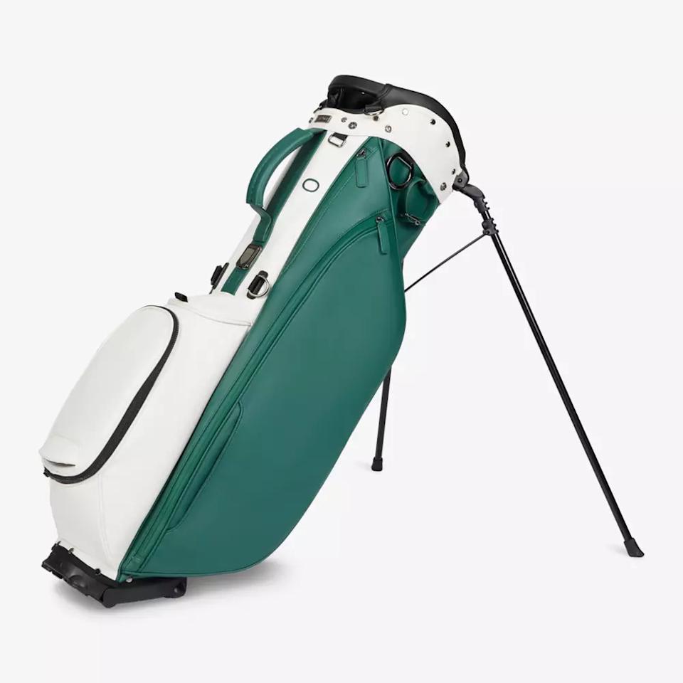A green and white golf bag with multiple compartments stands upright on extendable black legs, offering stability—an ideal choice for those seeking the best golf bags 2026 has to offer.