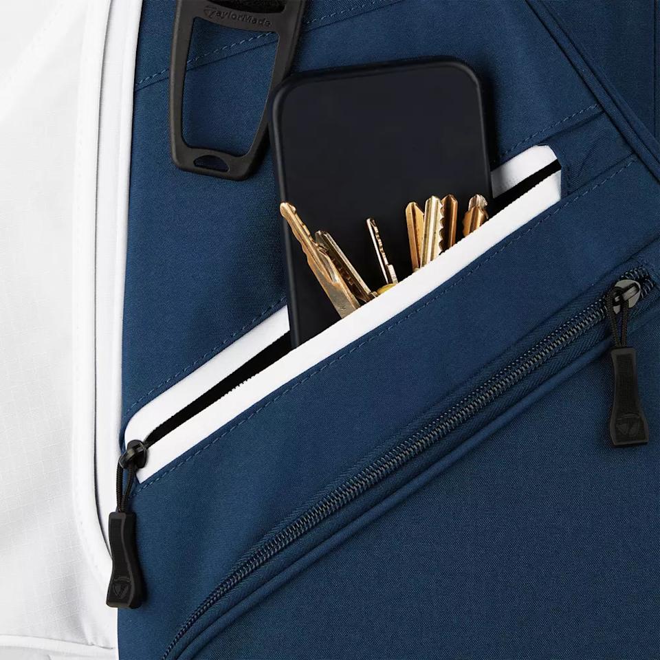 A close-up of a navy blue and white zippered pocket, found on one of the best golf bags 2026, holding a black smartphone and several gold keys on a keyring, with two zippers visible on the bag.