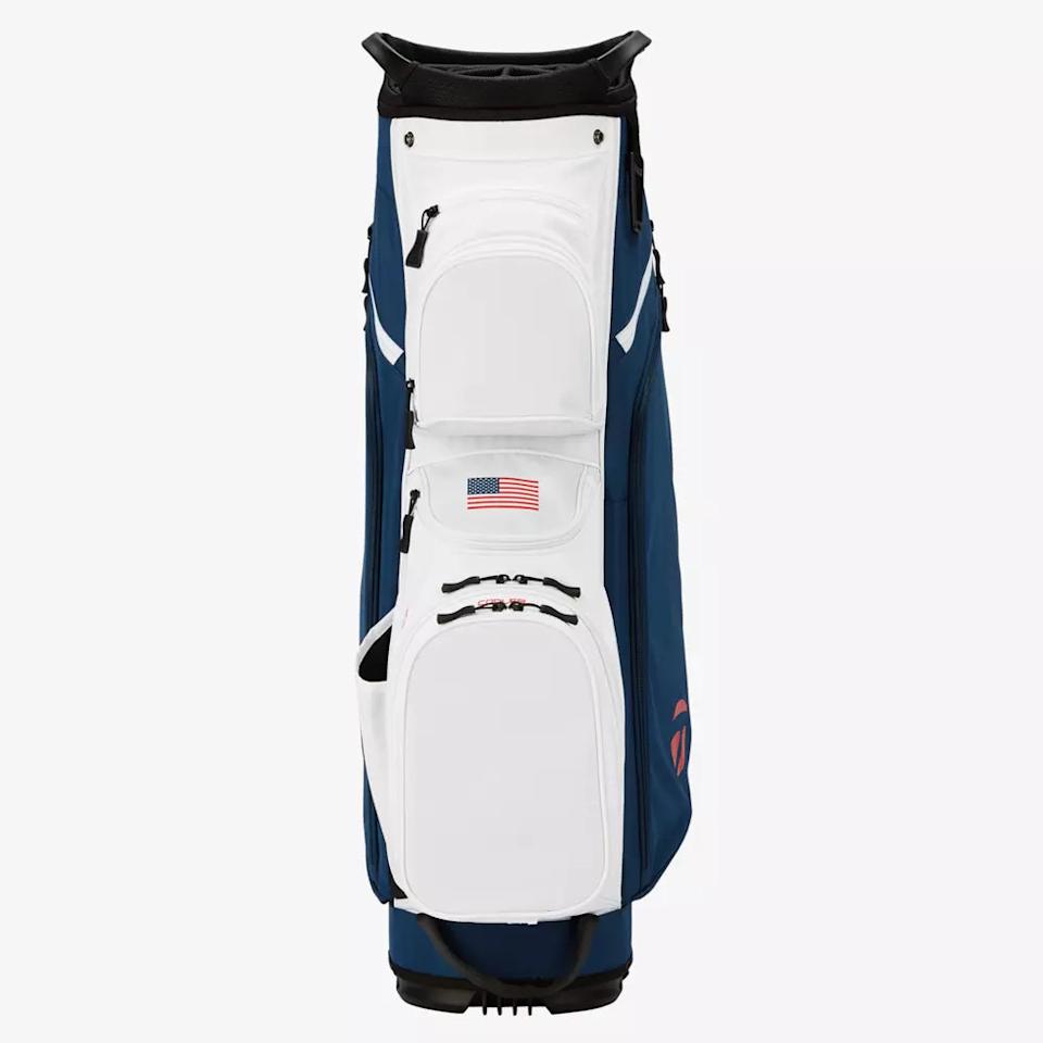 A white and blue golf bag with an American flag patch on the front pocket, shown standing upright against a plain white background—an ideal pick for those seeking the best golf bags 2026 has to offer.