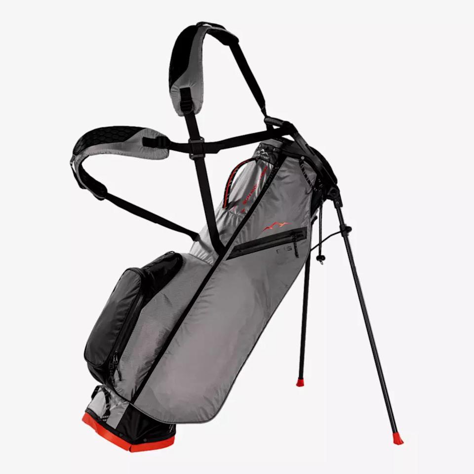 A lightweight gray golf bag with black and red accents stands upright on its two extended legs, featuring multiple pockets and padded dual shoulder straps—an excellent contender among the best golf bags 2026 has to offer.