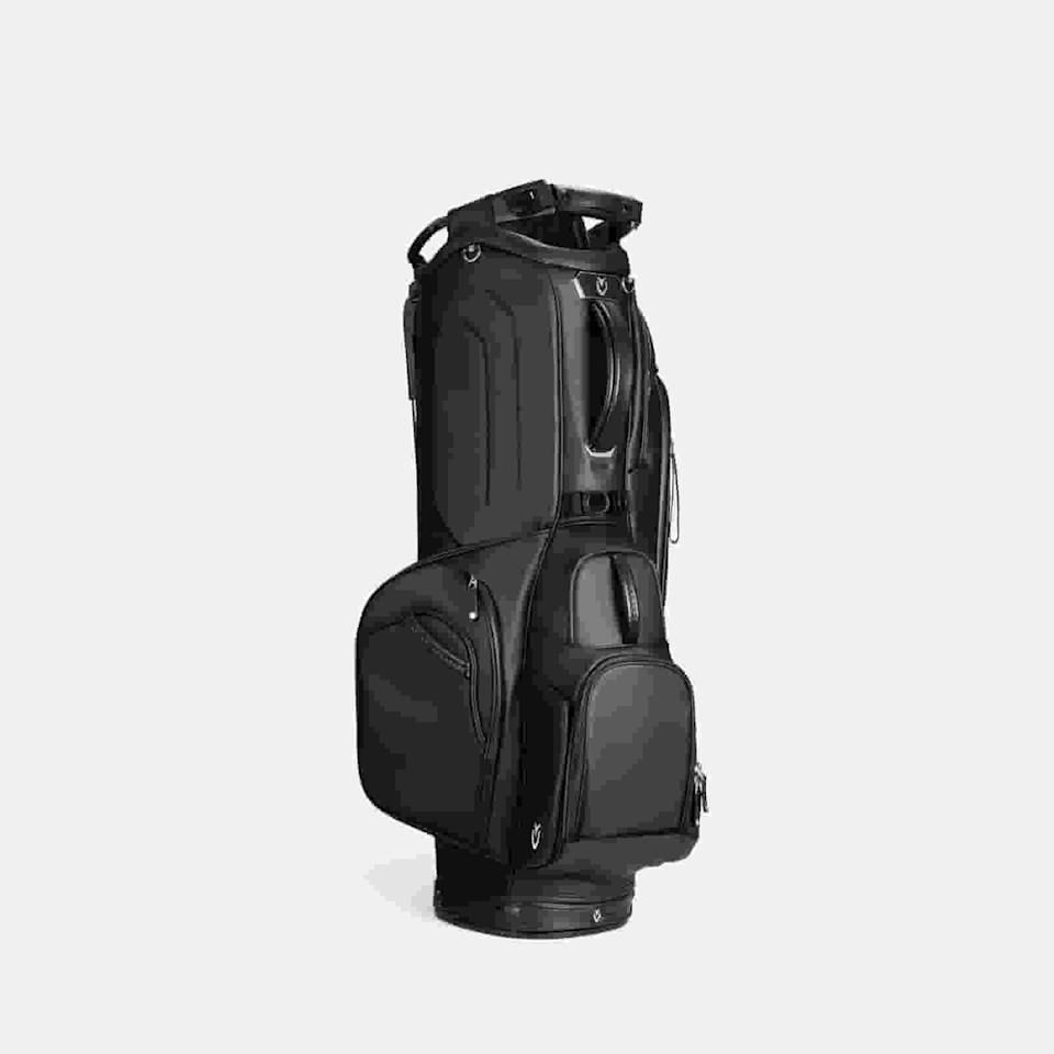 A black golf bag with multiple zippered pockets and compartments stands upright against a plain, light gray background—an ideal choice for those seeking the best golf bags 2026 has to offer.