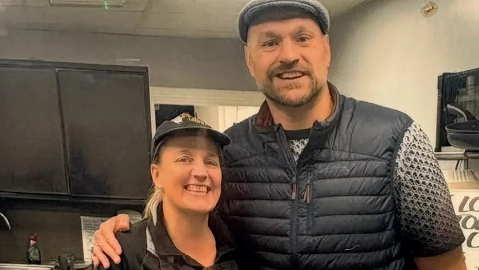 Rachel wears he Terry's Tato's uniform and stands next to Tyson who wears a farmer's cap and puffer gilet, they both smile brightly.