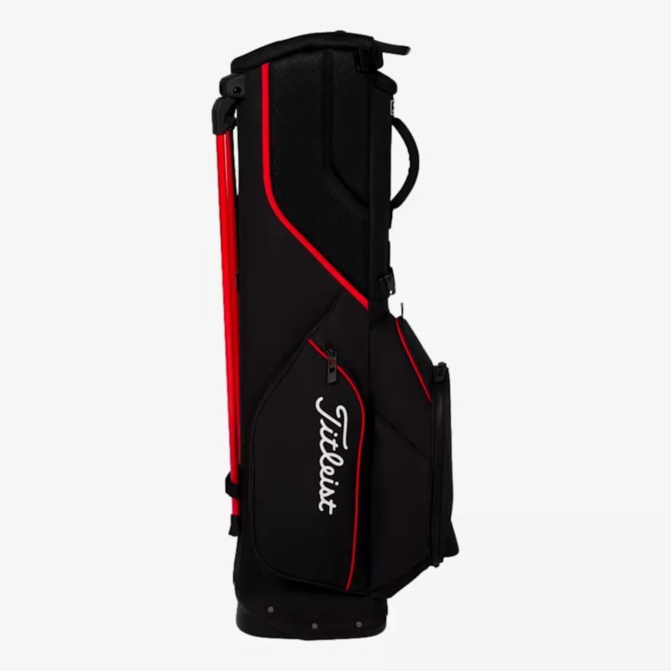 A black Titleist golf bag with red accents and white logo, featuring multiple pockets and a handle on top, stands upright against a plain white background—an example of the best golf bags 2026 can offer.