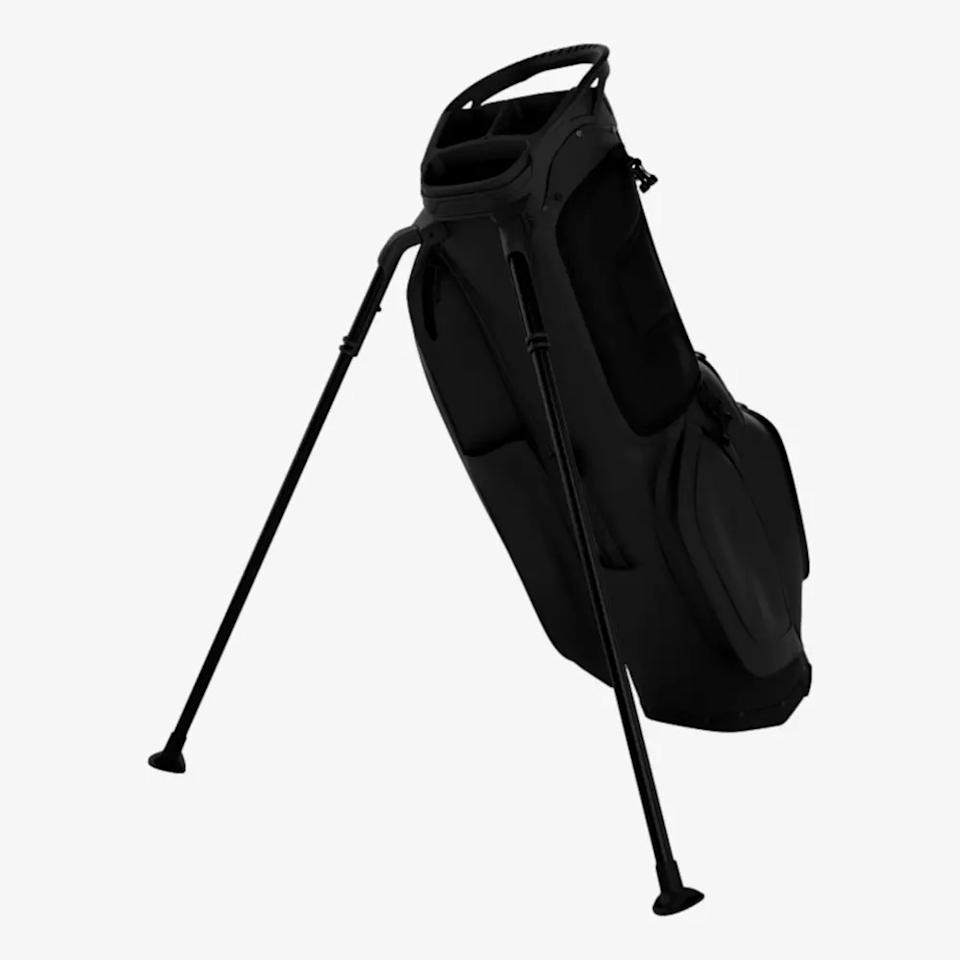 A black golf bag with a stand, featuring two extended legs to keep it upright. Ideal for those seeking the best golf bags 2026, it offers several pockets and a handle at the top. The background is plain white.