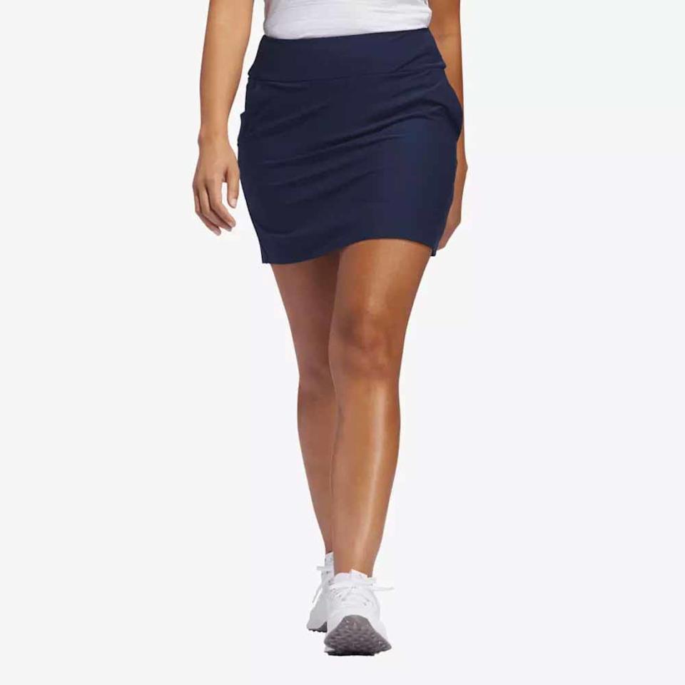 A person wearing a white top, navy blue athletic skirt, and white sneakers is walking forward against a plain light background—perfect apparel for stepping out in style this Mother’s Day.