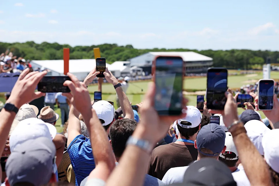 Jun 20, 2026; Southampton, New York, USA; Fans capture Scottie Scheffler as he tees off on one during the third round of the U.S. Open golf tournament at Shinnecock Hills Golf Club. Mandatory Credit: Bill Streicher-Imagn Images