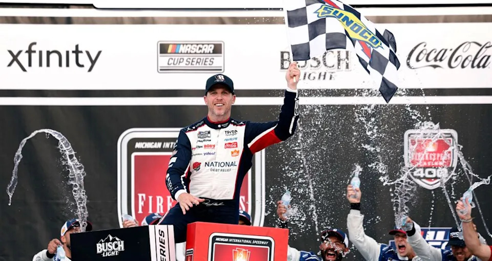 Denny Hamlin celebrates in Victory Lane at Michigan International Speedway following his NASCAR Cup Series win at the track.