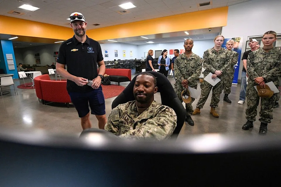 Shane van Gisbergen looks on as a U.S. Navy service member drives the NASCAR San Diego course on simulator