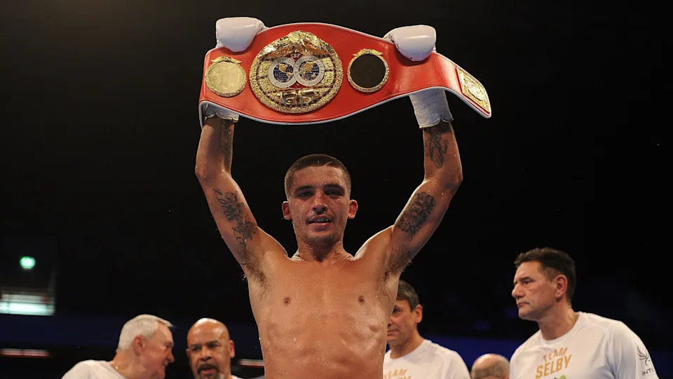 Selby holds aloft a red world title belt after a fight