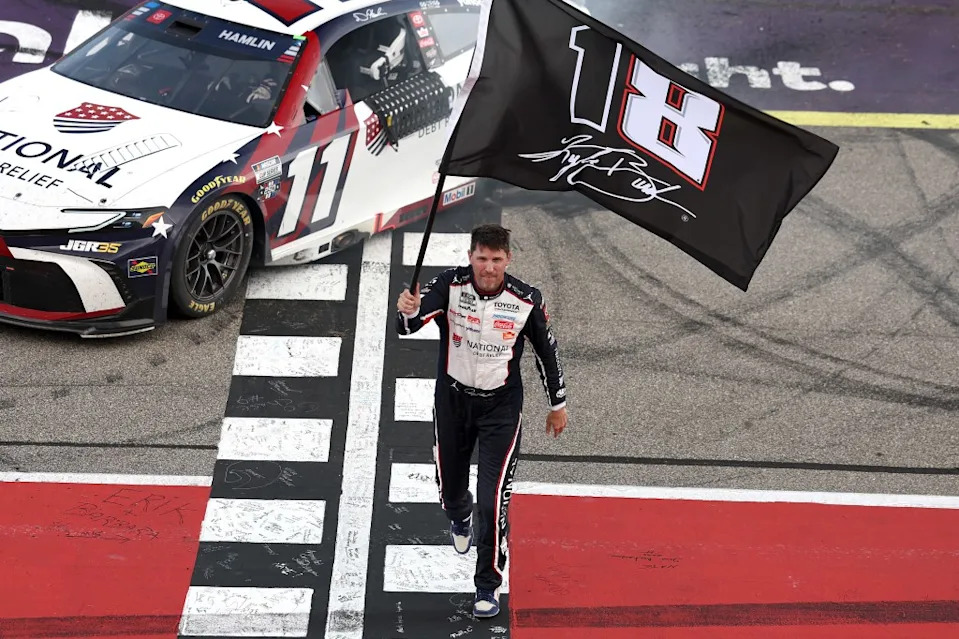 Denny Hamlin, driver of the #11 National Debt Relief Toyota, waves an 18 – 8 flag in honor of the late Kyle Busch after winning the NASCAR Cup Series FireKeepers Casino 400. Getty Images