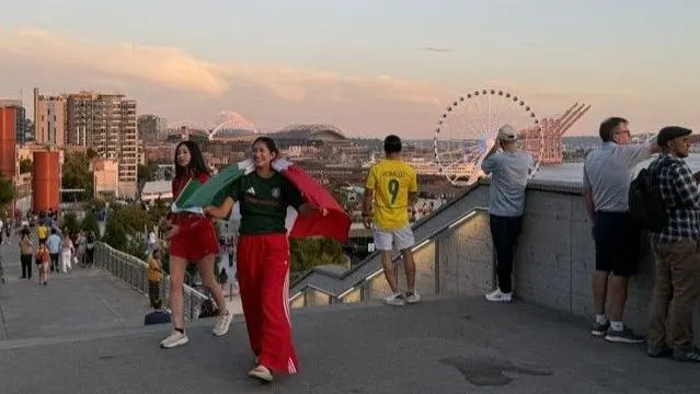 Football fans in different colour kits take in the view of the Seattle skyline from a high vantage point with a giant ferris wheel in the background.